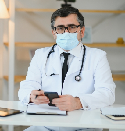A masked doctor with a stethoscope at a desk
